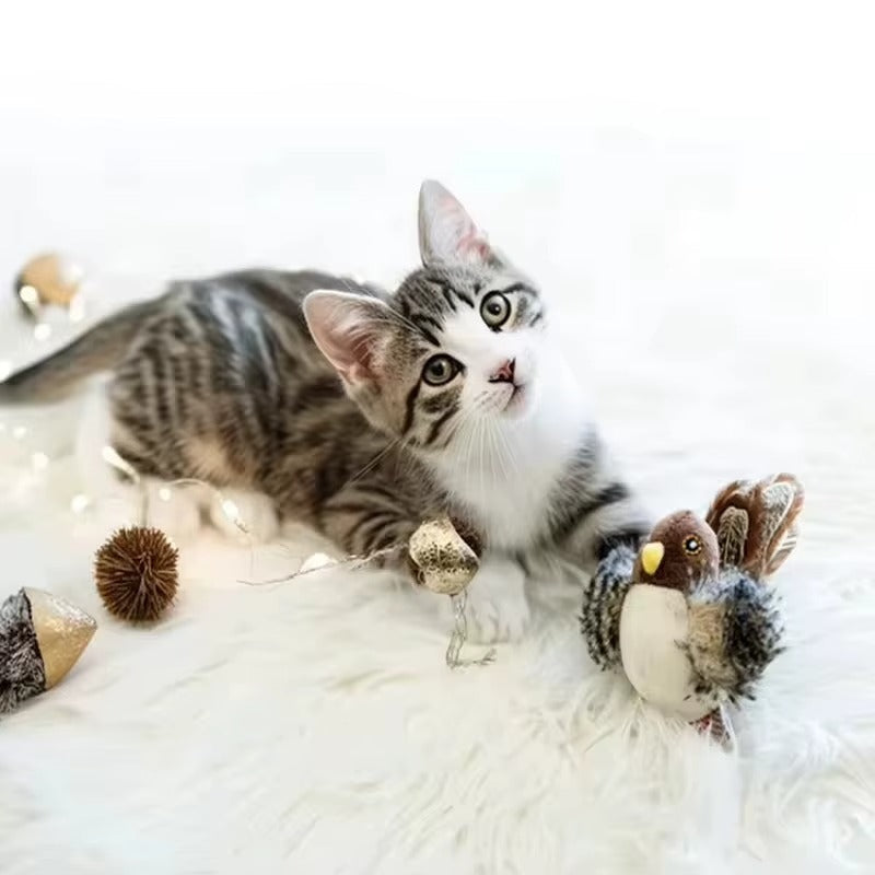 Tabby kitten beside chirping bird toy on soft white surface